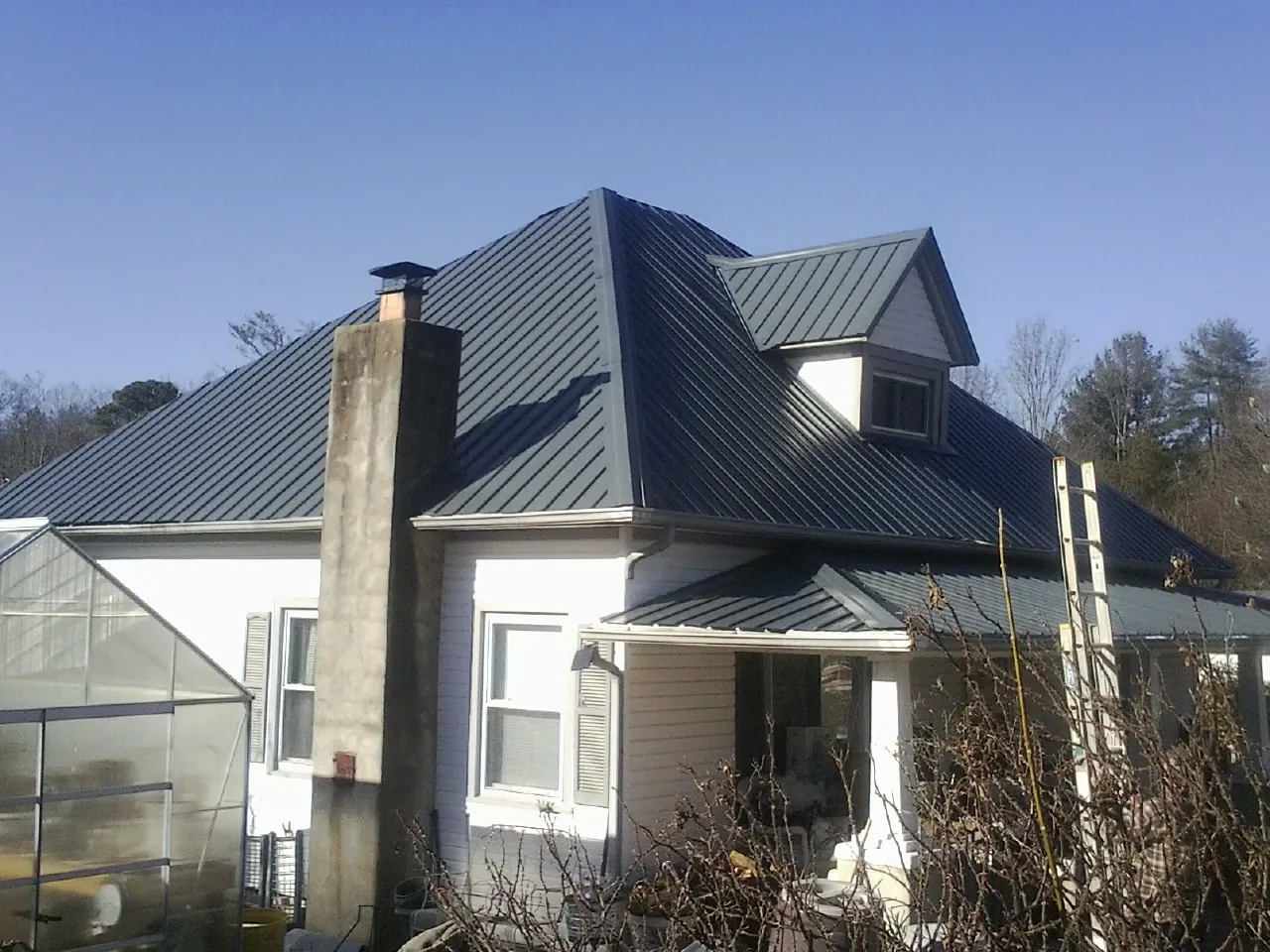 Dark blue standing seam metal roof on a white farmhouse with dormer — Slate & Tile Roof Repair by Roofing Brothers in Peculiar