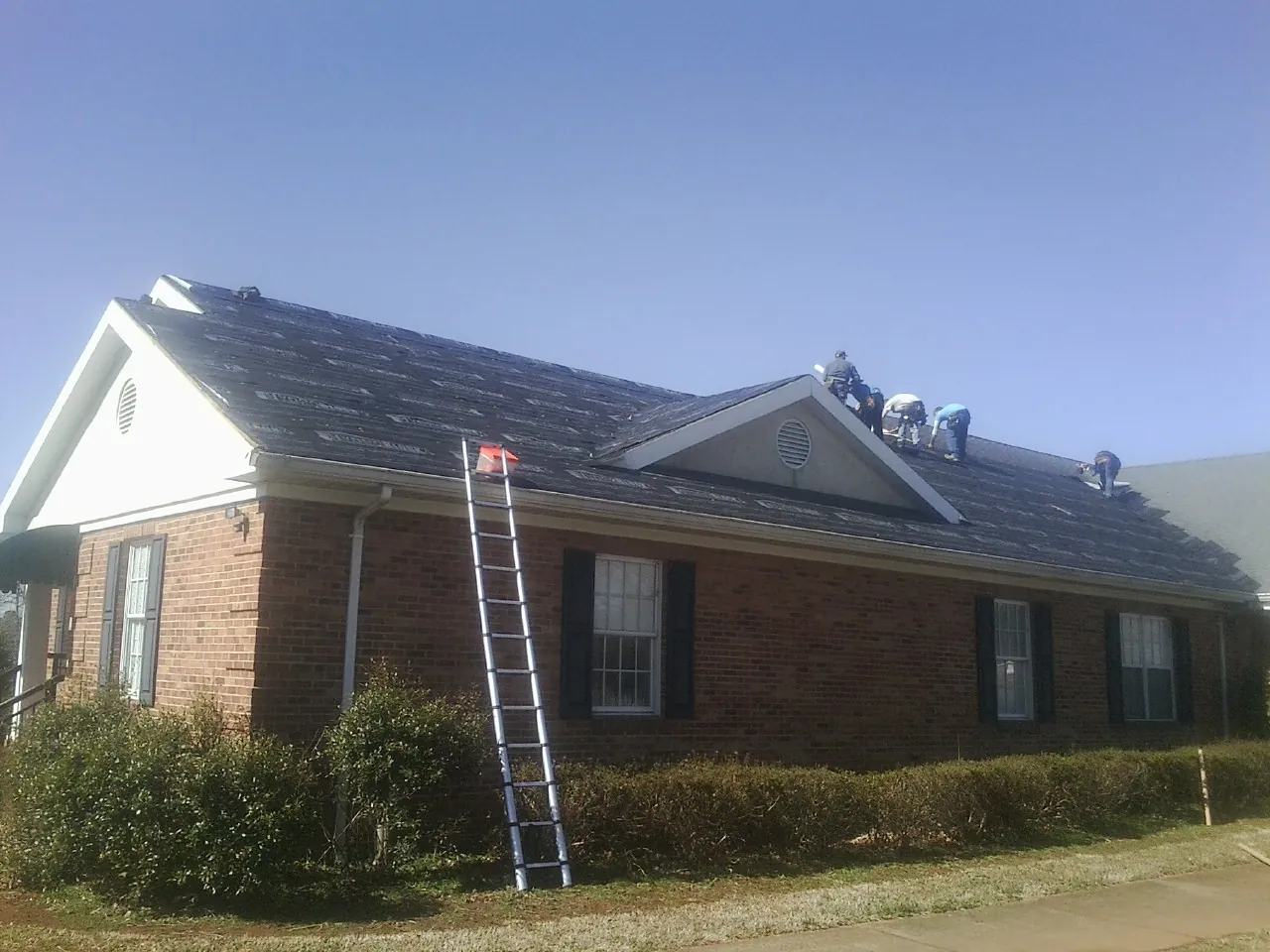 Crew tearing shingles off a brick ranch roof with a ladder set — Emergency Roof Repair work by our crew in Peculiar