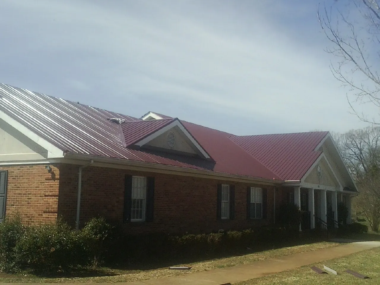 Red metal roof with gabled entries on a long brick building, from a Hail Damage Roof Repair job in Peculiar