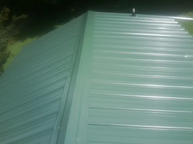 New green metal panels meeting at the ridge of a roof — Flat Roof Repair work by our crew in Peculiar