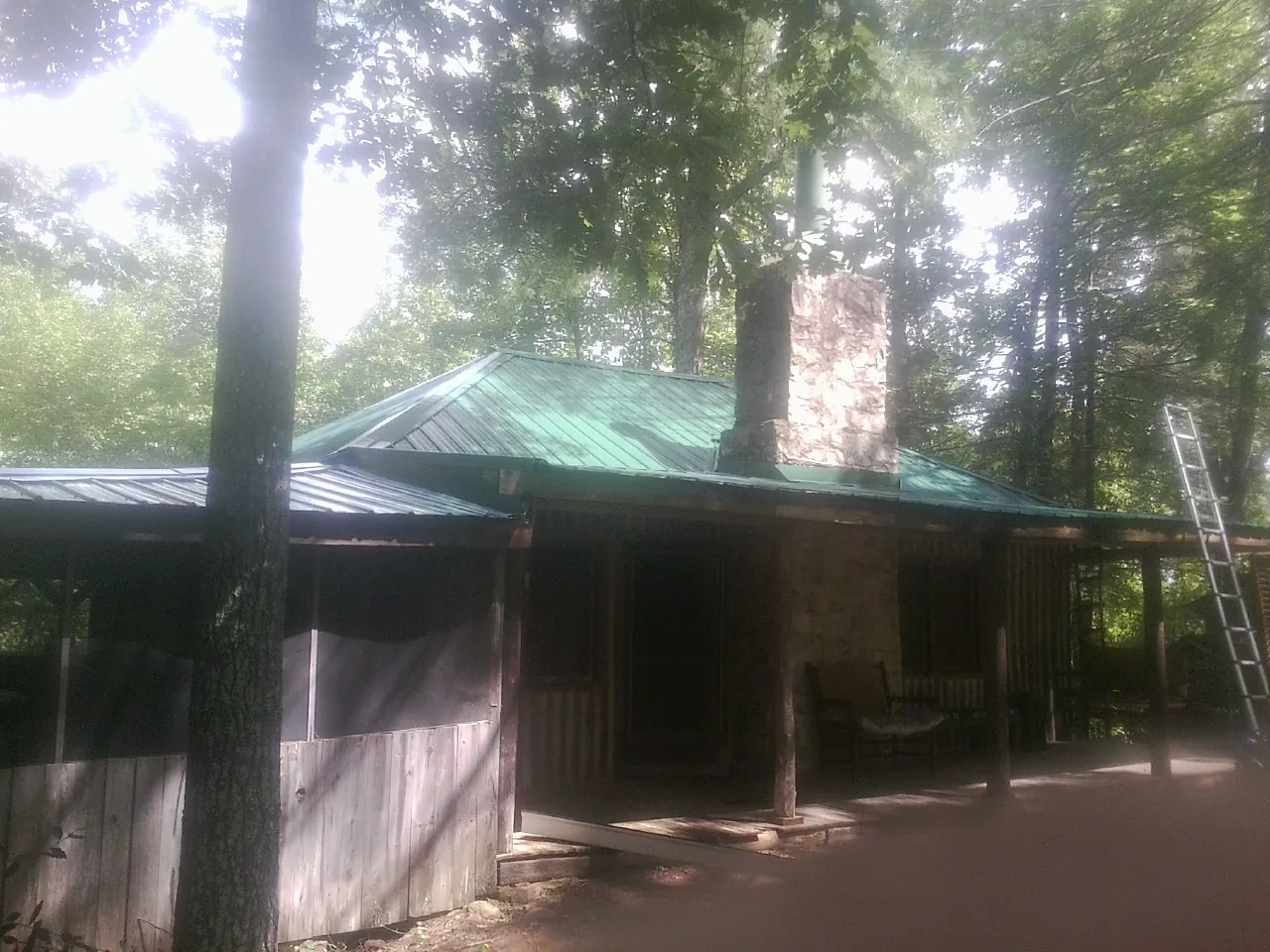 Green metal roof and stone chimney above a log cabin porch in Peculiar