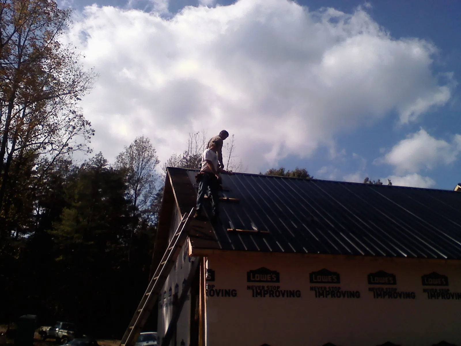 Roofer fastening dark metal panels high against a cloudy sky, from a Roof Inspection job in Peculiar
