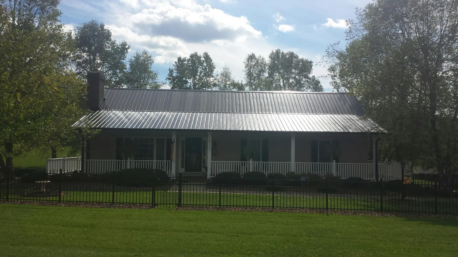 Gray metal roof on a brick ranch with a full width front porch — Gutter Guard Installation work by our crew in Peculiar