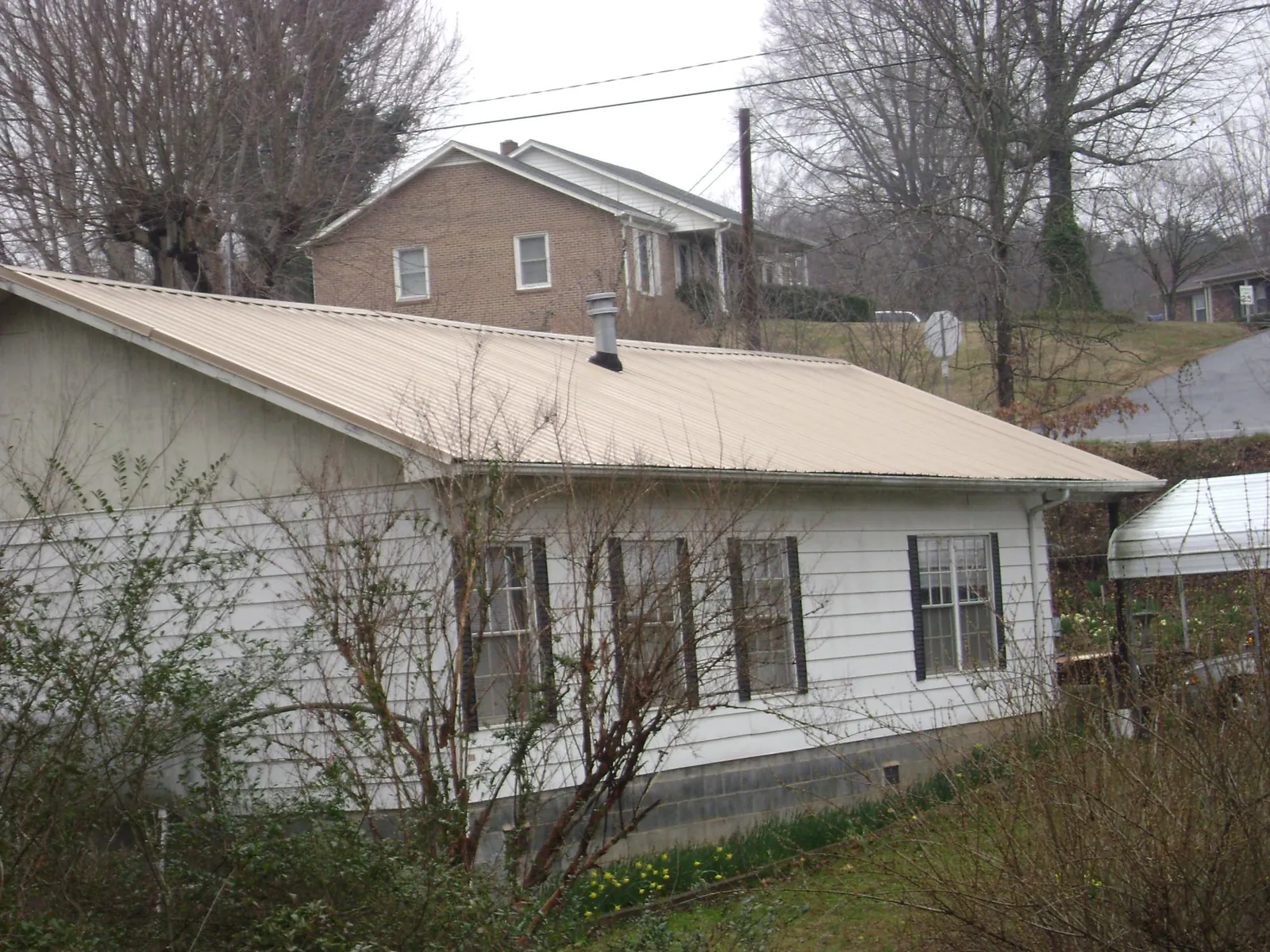 Tan metal roof on a white sided house set into a hillside — Commercial Roofing by Roofing Brothers in Peculiar