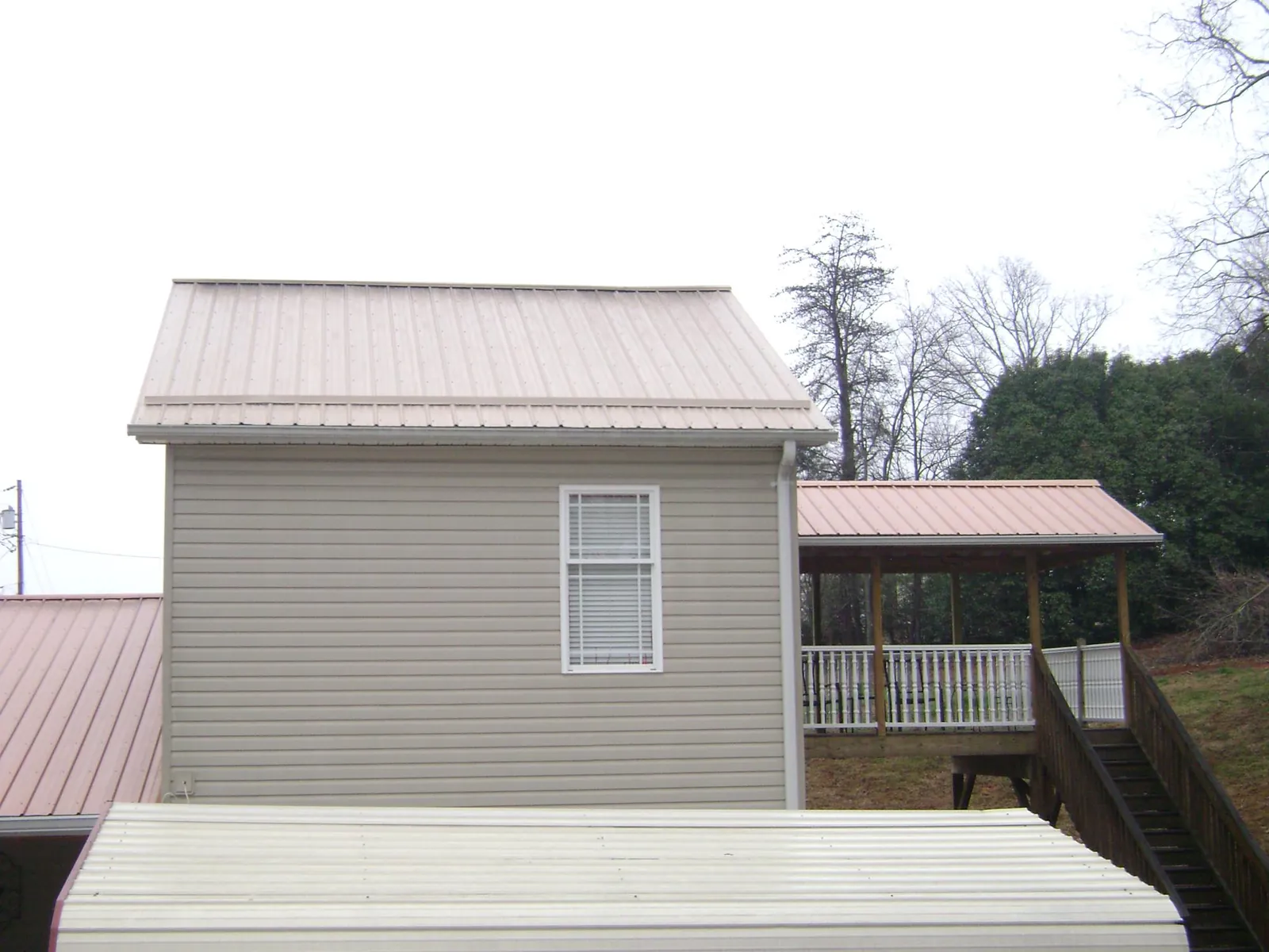 Tan metal roofs on a two story addition and attached porch, from a Roof Replacement job in Peculiar